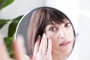 Woman examining her face in a round mirror
