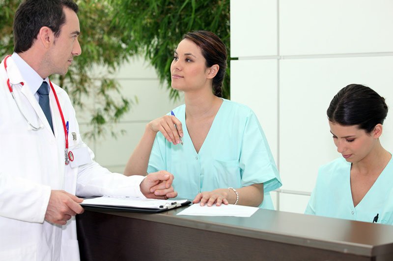 Male physician talking to his staff at reception desk