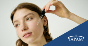 Woman applying eye drops with a dropper; blue logo panel in the bottom-right reads IAPAM