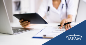 Healthcare professional in a white coat reviews documents with a tablet on a desk; TAPAM logo in the corner.